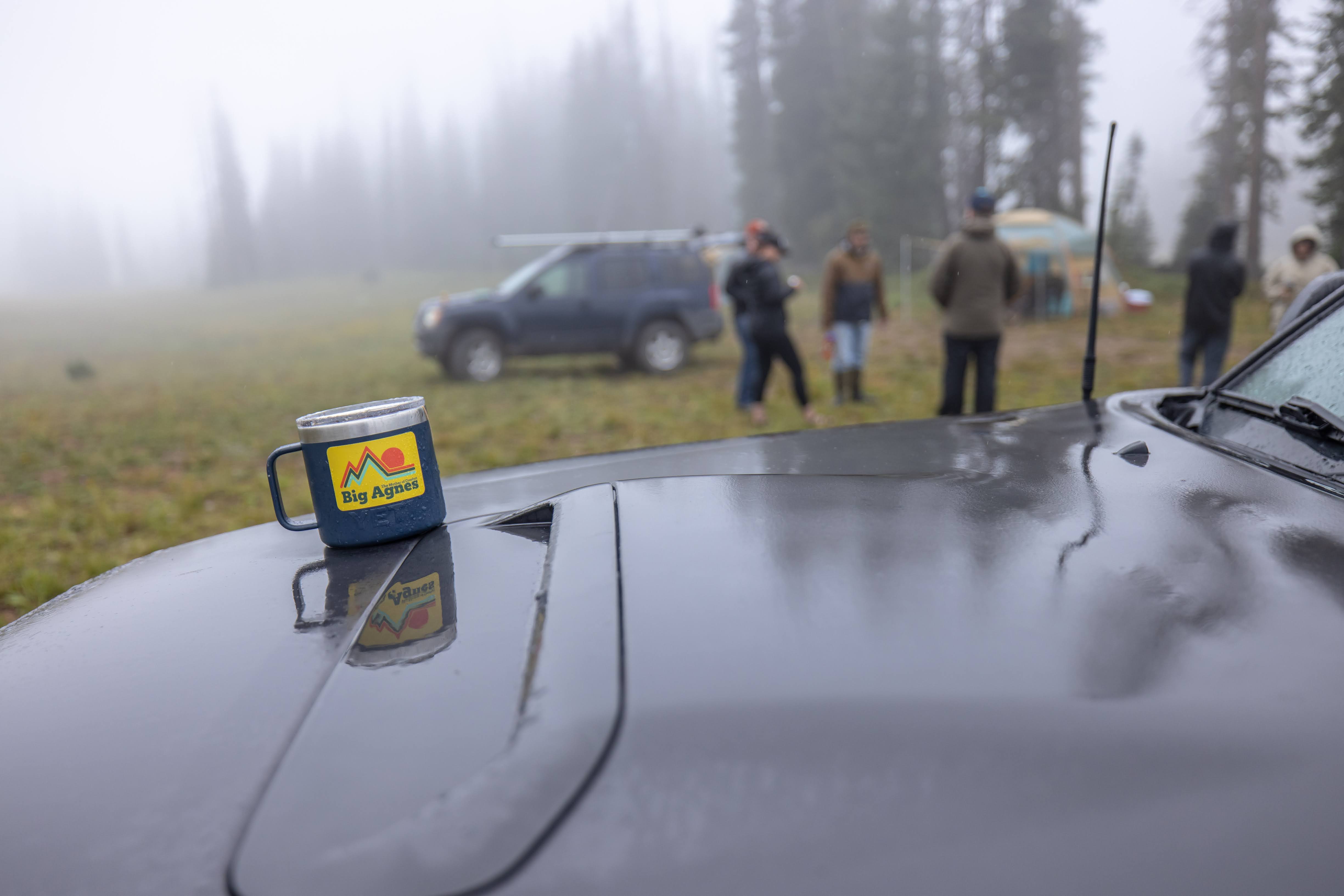 A mug on a car hood overlooking a rainy campground