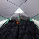 Person lying inside a tent with sleeping bags and a black quilt