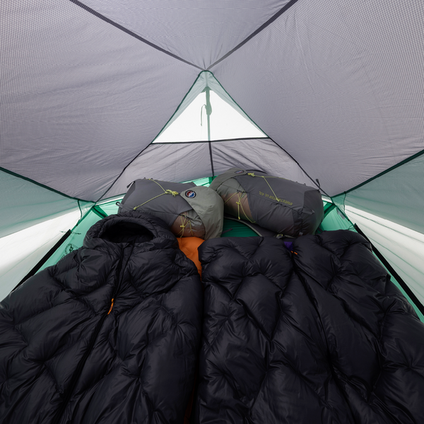Person lying inside a tent with sleeping bags and a black quilt